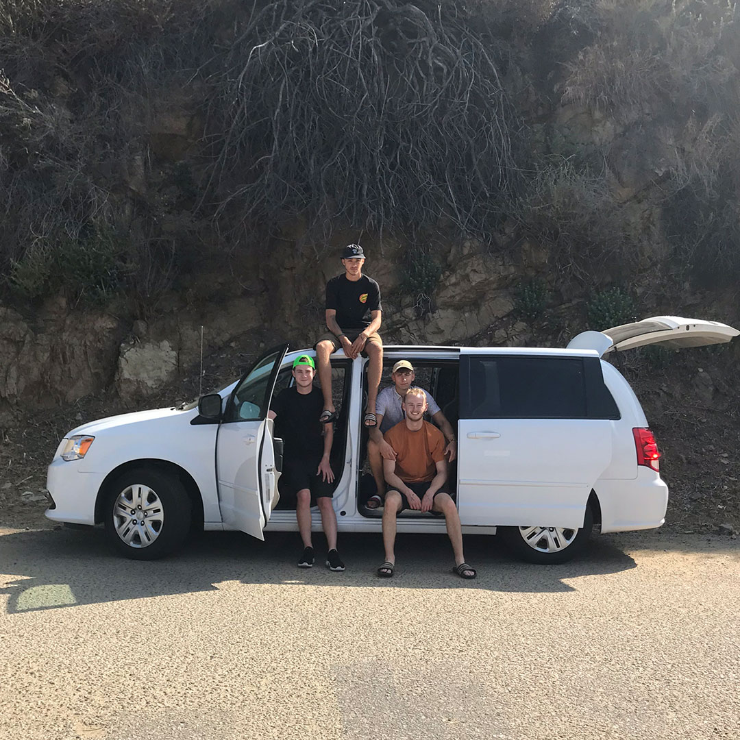 A group of boys sitting on top of their car on their roadtrip 